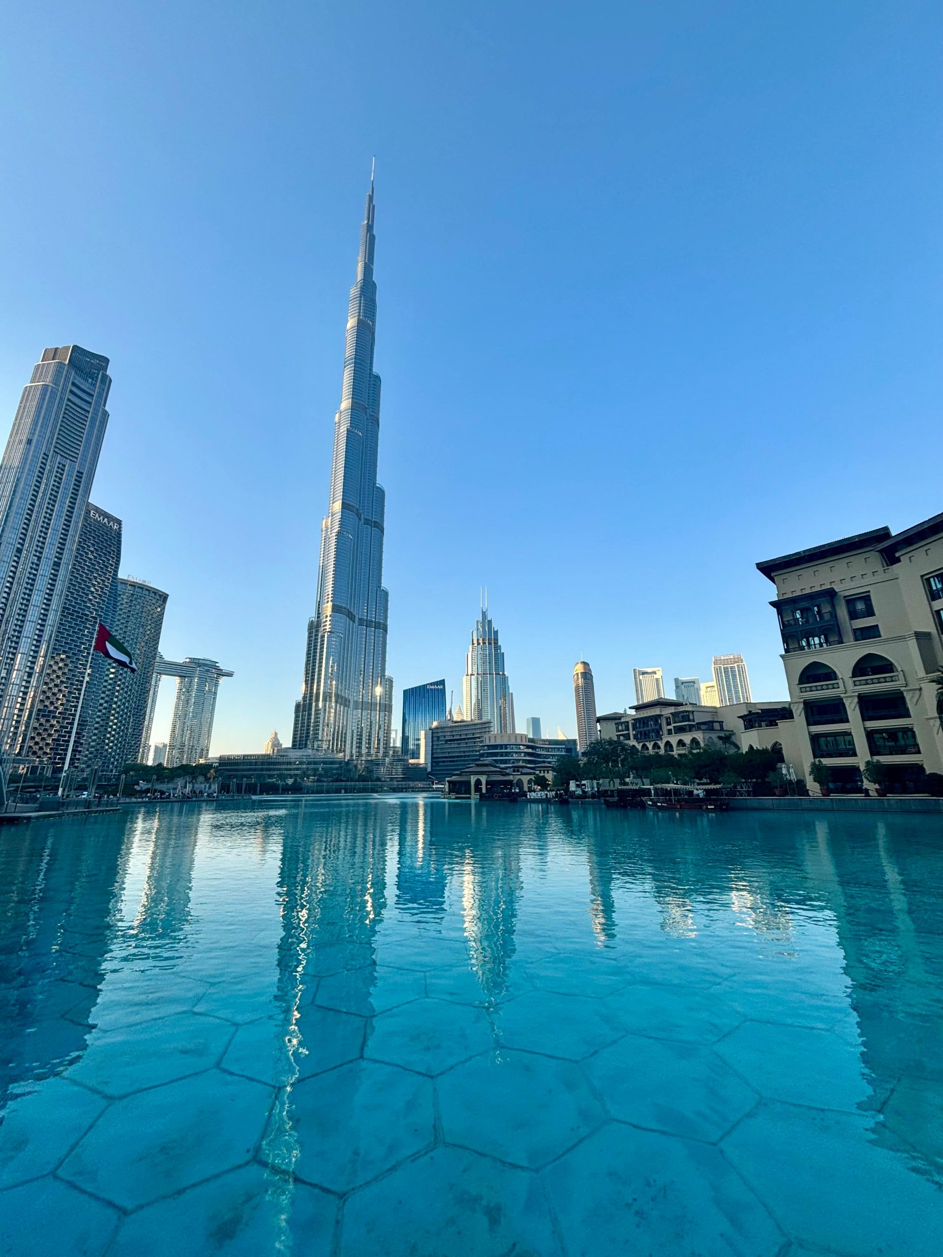 Capture the iconic Burj Khalifa and Dubai skyline with a serene water reflection under a clear blue sky.